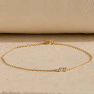 Bracelet fin en titane doré avec petite pierre de naissance rectangulaire sertie, style minimaliste.