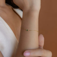 Bracelet fin en titane doré avec petite pierre verte carrée, style minimaliste et léger.