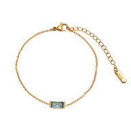 Bracelet fin en titane doré avec pierre de naissance rectangulaire bleu clair et chaîne ajustable.