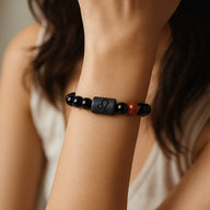 Bracelet en perles de verre noir et une perle rouge, avec symbole astrologique gravé sur une plaque centrale noire, style.