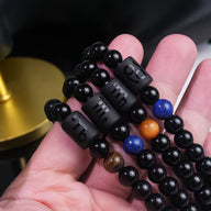 Bracelet double rang en perles de verre noir lisses avec quatre perles rectangulaires noires gravées de symboles.