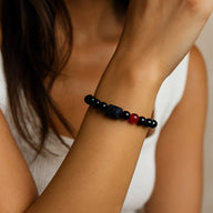 Bracelet en perles de verre noir avec une perle rouge centrale et un symbole astrologique gravé sur une perle noire mate.