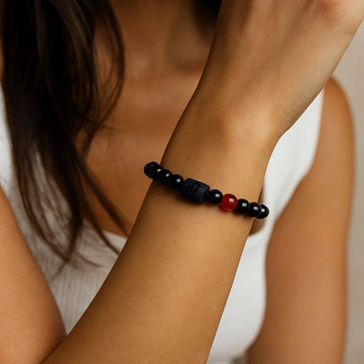 Bracelet en perles de verre noir avec une perle rouge centrale et un symbole astrologique gravé sur une perle noire mate.