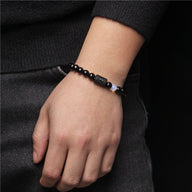 Bracelet en perles de verre noir avec symbole astrologique argenté, style sobre et élégant sur poignet.