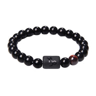 Bracelet perles rondes en verre noir avec perle cylindrique matte gravée du symbole astrologique Capricorne, accent marron.