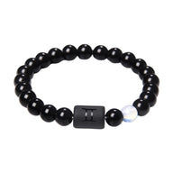 Bracelet perles rondes en verre noir avec une perle blanche translucide et une plaque noire gravée du symbole astrologique.