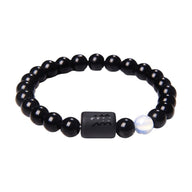 Bracelet élastique perles de verre noir rondes, une perle blanche nacrée, breloque rectangulaire noire avec symbole.