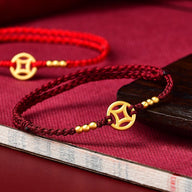 Bracelet fil rouge bordeaux tressé avec pendentif doré symbolique et perles dorées.