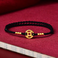 Bracelet fin en fil rouge noir tressé avec pendentif doré rond orné d’un motif ajouré et perles dorées.