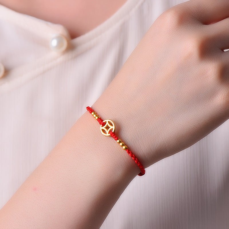 Bracelet en nylon rouge avec médaille dorée et perles dorées, style porte-bonheur, porté au poignet.