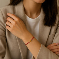 Bracelet fil rouge fin avec perle dorée porté au poignet, style minimaliste et élégant.