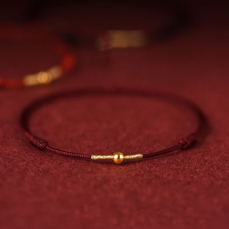 Bracelet fil rouge bordeaux avec perle dorée centrale en nylon, style minimaliste et ajustable.