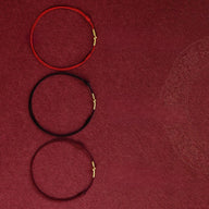 Trois bracelets en fil rouge, noir et bordeaux avec fermoirs dorés, style minimaliste.