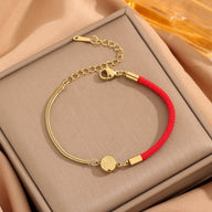 Bracelet femme fil rouge et titane doré avec médaille ronde gravée et chaîne réglable.