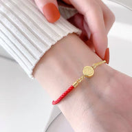Bracelet femme en fil rouge torsadé avec détail en titane doré et médaille gravée ronde.