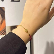Bracelet fin en fil rouge avec un petit médaillon en titane doré porté au poignet féminin.