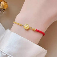 Bracelet fin en fil rouge avec médaillon en titane doré gravé d’un symbole chanceux.