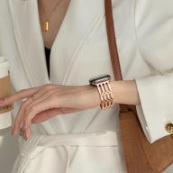 Bracelet Apple Watch or rosé à maillons larges porté avec veste blanche chic.