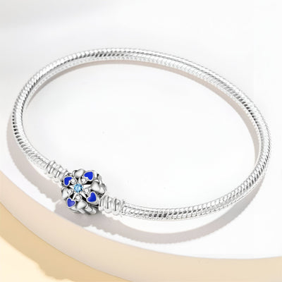 Bracelet argenté serpent avec charm fleur sertie de pierres bleues, style personnalisable pour femme.