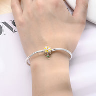 Bracelet argent fin avec charm chrysanthème jaune et détails délicats porté au poignet.