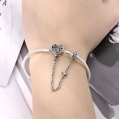 Bracelet argenté fin avec chaîne de sécurité et fermoir cœur ajouré sur poignet féminin.