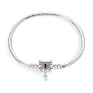 Bracelet argenté pour charm avec pendentif cœur cadenassé orné de pierres violettes et clé pendante.