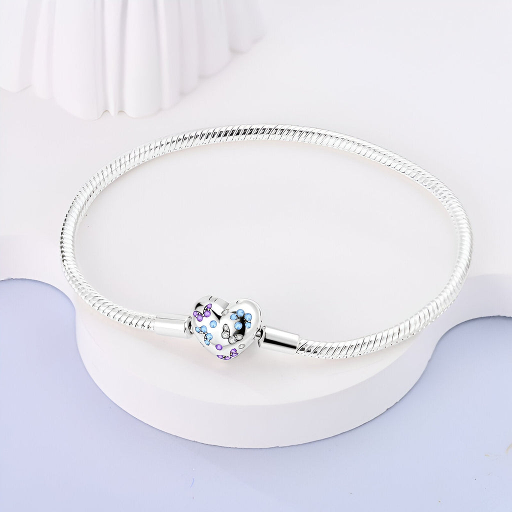 Bracelet argenté fin pour charms avec fermoir cœur orné de papillons bleus et violets.