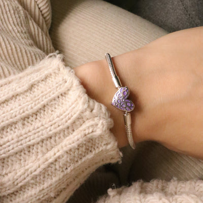 Bracelet argenté fin avec un charm cœur violet lumineux texturé porté sur poignet féminin.