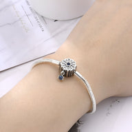 Bracelet argenté pour charm avec pendentif fleur et petit charm bleu sur poignet féminin.