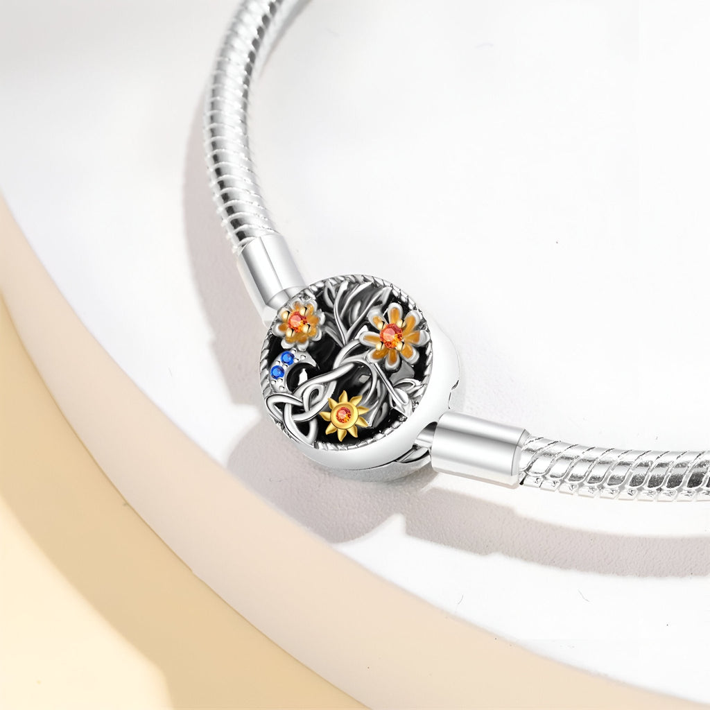 Bracelet argenté à maillons avec charm rond noir orné de fleurs orange, jaunes et une petite pierre bleue.
