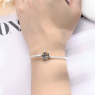 Bracelet argent fin avec charm rond motif floral noir et or, style minimaliste élégant.