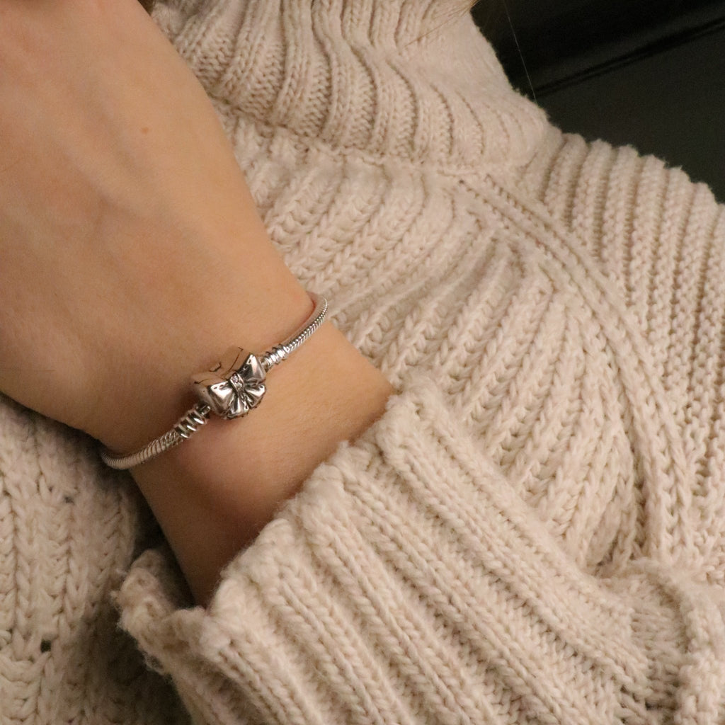 Bracelet fin en cuir beige avec nœud ruban en métal argenté, style délicat pour femme.