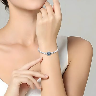 Bracelet argenté fin avec charm œil bleu au centre, porté au poignet d’une femme.