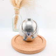 Bracelet argenté avec charms papillon bleu et breloques scintillantes sur présentoir métallique rond.