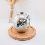 Bracelet argenté fin avec charms personnalisables en forme de cœur, étoile, émotion et breloque en bleu et noir posé sur un.