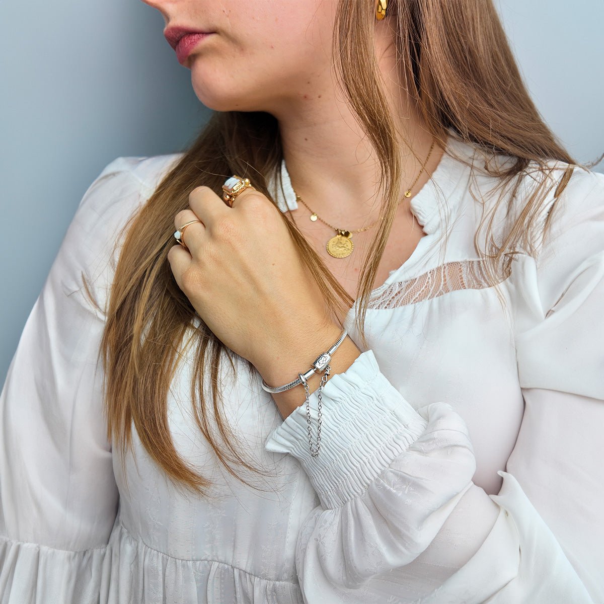 Bracelet fin argenté pour charms, chaîne délicate avec fermoir élégant, porté avec bague et collier doré sur femme en blouse