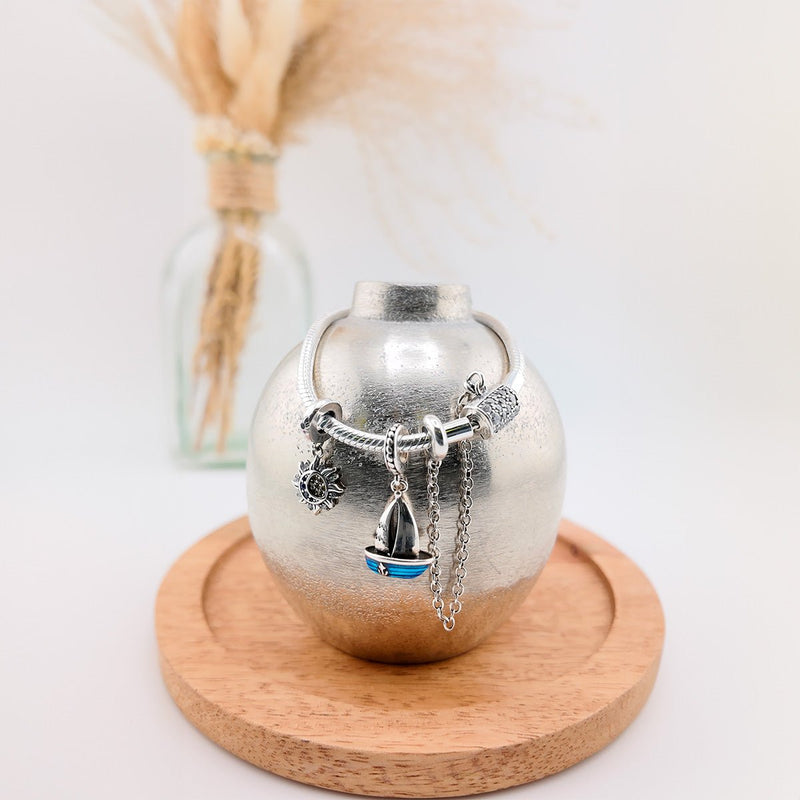 Bracelet argenté pour charm avec pendentifs, dont un bateau bleu, design fin et personnalisable.