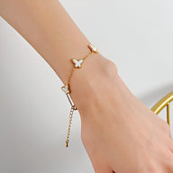 Bracelet en acier inoxydable doré avec charms papillons blancs délicats sur poignet féminin.