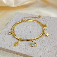Bracelet femme en acier inoxydable doré avec charms œil, étoile et coquillage sur chaîne fine.