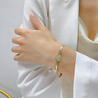 Bracelet doré en acier inoxydable avec cœur serti de zirconium sur poignet féminin.