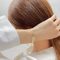 Bracelet doré fin en acier inoxydable avec cœur serti de zirconium porté au poignet féminin.