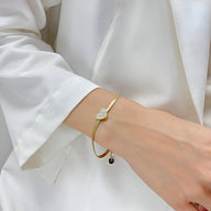 Bracelet fin doré en acier inoxydable avec cœur serti de zirconium porté au poignet féminin.