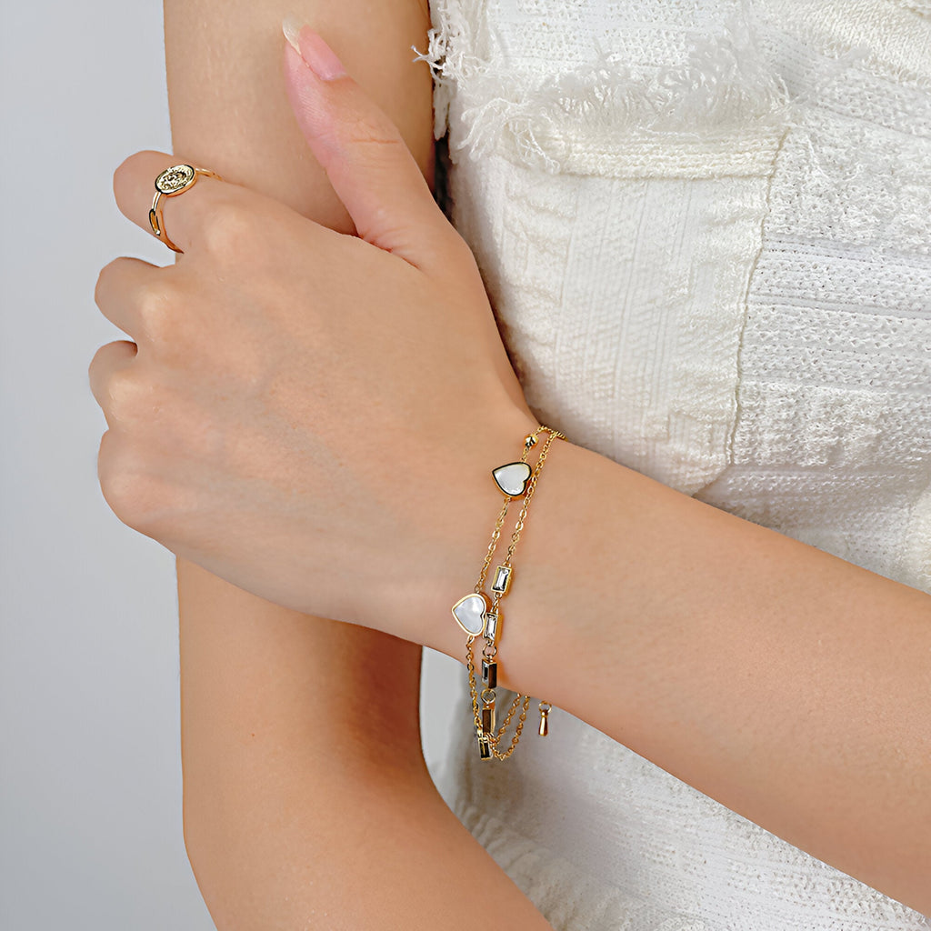 Bracelet or en acier inoxydable avec cœurs blancs et zirconium, porté au poignet féminin.