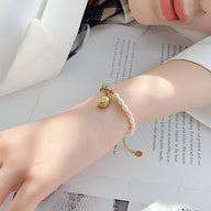 Bracelet femme en acier doré avec perles blanches et charm smiley en métal sur poignet.