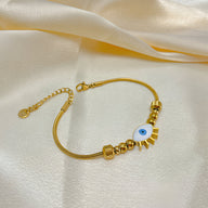 Bracelet femme doré en acier inoxydable avec œil bleu central et pampilles en forme de rayons.
