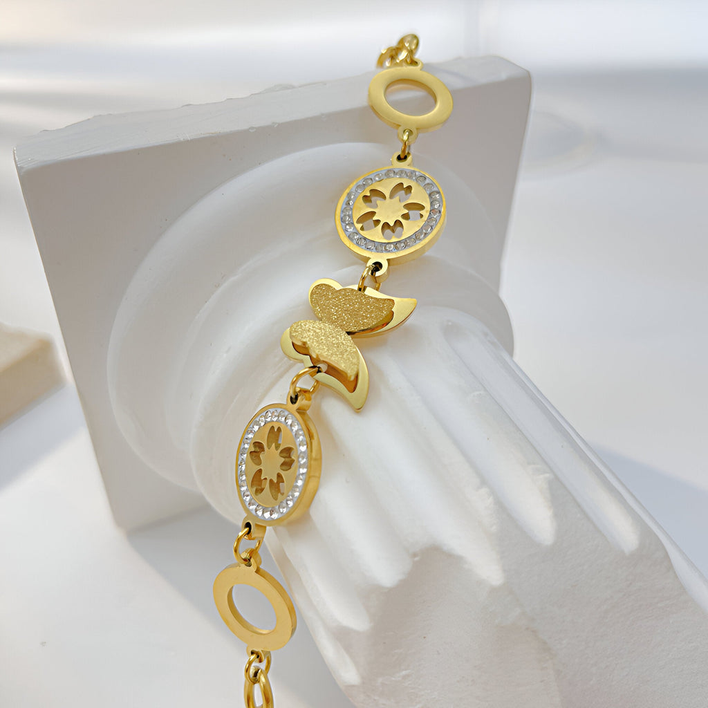 Bracelet femme en acier inoxydable doré avec papillon et éléments floraux ajourés.