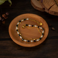 Bracelet femme en acier doré avec perles noires, blanches et pierres naturelles, chaîne fine réglable.