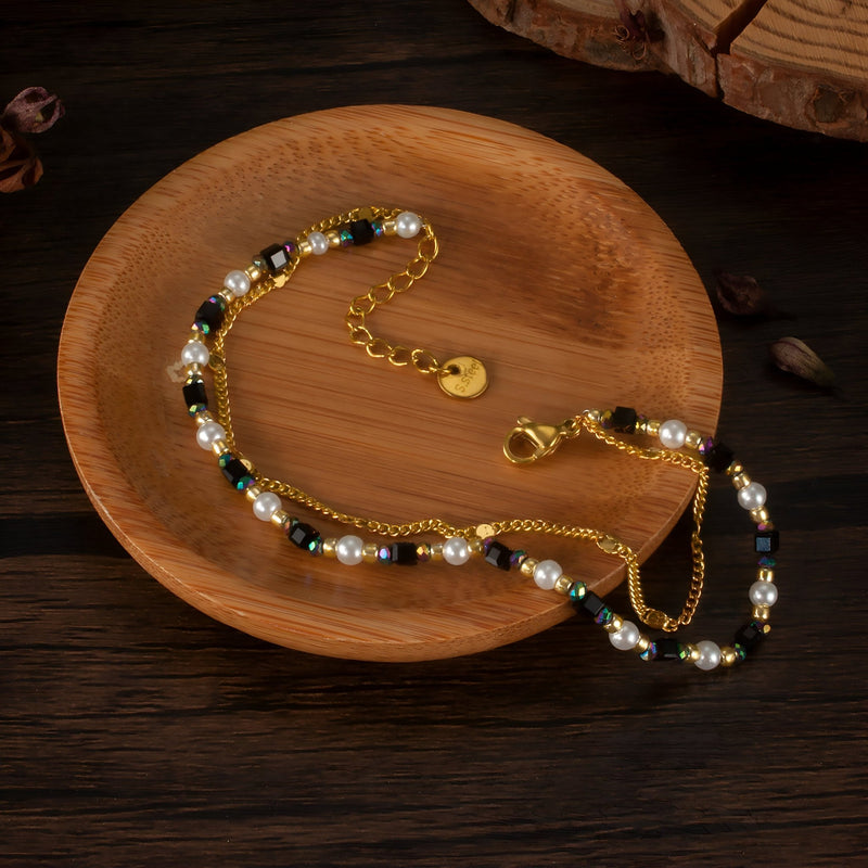 Bracelet femme en acier inoxydable doré avec pierres naturelles vertes et perles blanches sur plateau en bois.