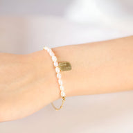 Bracelet femme en acier inoxydable or avec perles blanches et pendentif rectangulaire doré.