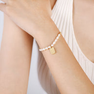 Bracelet pour femme en acier inoxydable perlé avec pendentif rectangulaire doré.